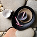 A Libbey sand matte porcelain saucer with a white coffee cup on a stone surface with a slice of dragon fruit on it.