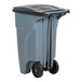 A grey Rubbermaid commercial trash can with black wheels and a black lid.