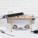 A Vollrath Classic Brass Trim electric chafing dish on a table with food in it.
