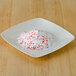 A white bowl filled with Rokz peppermint cocktail rimming sugar with red crystals on top.