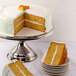 A Cal-Mil stainless steel cake stand with a slice of cake on a plate.