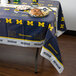 A table covered with a University of Michigan Wolverines themed tablecloth with food on it.