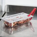 A clear plastic container with food inside and a clear plastic lid with a spoon notch on a counter.