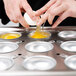A person's hand breaking an egg into a Vollrath egg poacher cup.