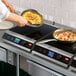 A chef using a Hatco countertop induction range to cook food in a pan.