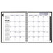 A black DayMinder hardcover monthly planner open to a white calendar page.