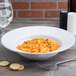 A white melamine bowl of pasta with sauce on a table.