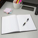 An Adams black four column account notebook on a desk with a pen.