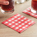 A hand holding a glass of beer over a red and white gingham napkin.