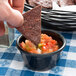 A person holding a chip dips it into a black ramekin of salsa.