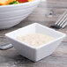 A white Elite Global Solutions squared melamine bowl filled with salad next to a bowl of white sauce.