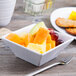 An Elite Global Solutions white squared melamine bowl filled with fruit on a table.