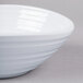 An Elite Global Solutions white melamine bowl with a curved edge on a gray surface.