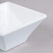 An Elite Global Solutions white square melamine bowl on a gray surface.