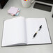 A black Adams Three Column account notebook with a pen on top.