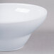 A close-up of an Elite Global Solutions white melamine bowl with a dome bottom and a handle.