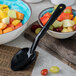 A Carlisle black solid serving spoon in a bowl of fruit.