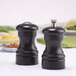 Two black Chef Specialties Capstan pepper mills on a table.