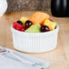 A bowl of fruit in a white Tuxton ramekin on a table.