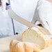 A person in white gloves using a Mercer Culinary purple bread knife to cut a loaf of bread.