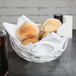 A white HS Inc. open weave basket filled with rolls on a table with a soda.