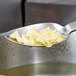 A Vollrath stainless steel spoon with noodles on it over a pot of water.