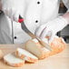 A person in white gloves using a Mercer Culinary Millennia Colors® red bread knife to slice bread.