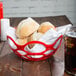 A close up of a red open weave basket filled with rolls on a table.