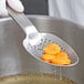 A gloved hand using a Vollrath heavy-duty perforated spoon to serve carrots.