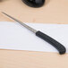 A Westcott letter opener with a black handle and stainless steel serrated blade opening a white envelope.