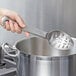A hand holding a Vollrath stainless steel slotted spoon over a pot.