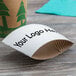 A white customizable cardboard coffee cup sleeve with black text on a table with a white coffee cup.