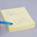 A hand writing "3M Canary Yellow Post-It" on a Post-It note with a blue pen.