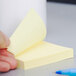 A person's hand holding a 3M Canary Yellow Post-It note.