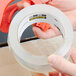 A hand holding a roll of 3M Scotch clear heavy-duty shipping and packaging tape.