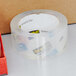 A roll of 3M Scotch clear heavy-duty shipping tape next to a box.