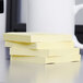 A stack of 3M Canary Yellow fan-folded Post-It Notes on a table.