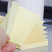 A hand holding a fan-folded stack of 3M Canary Yellow Post-It Notes.