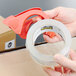 A hand holding a roll of 3M Scotch clear heavy-duty shipping tape.
