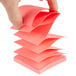 A hand holding a stack of neon pink 3M Post-It notes.