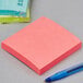 A pink Post-It note next to a blue pen.