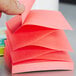 A hand holding a fan-folded stack of neon pink Post-It notes.