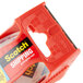 A red 3M clear plastic container of 6 Scotch heavy-duty packaging tape rolls with a tape dispenser.