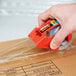 A hand using a red 3M tape dispenser to seal a box.