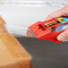 A hand using a red 3M Scotch heavy-duty packaging tape dispenser to cut a box.