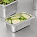 A stainless steel Choice 1/9 size steam table pan with cucumbers in it.