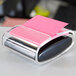 A 3M Post-it note holder with a pink sticky note on it.