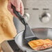 A person using a Vollrath high heat nylon slotted turner to cook salmon in a pan.
