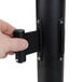 A person using an Aarco black crowd control stanchion with black retractable belts.