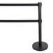 A black metal Aarco crowd control stanchion with dual black retractable belts.